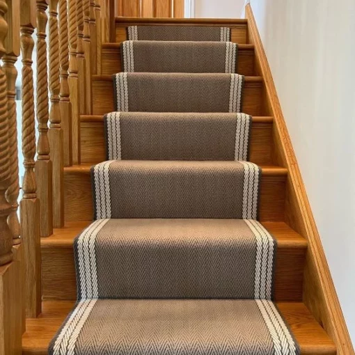Tapis tissé plat beige, gris et blanc installé sur un escalier droit en bois.