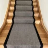 Tapis d'escalier tissé plat avec motif en chevron noir et blanc et bordure tressée noire, installé sur un escalier droit en bois.