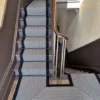 Tapis d'escalier avec motif en chevron noir et blanc et bordure tressée noire, installé sur des volées droites d'escaliers en bois et un palier.