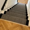 Tapis d'escalier avec motif en chevron noir et blanc et bordure tressée noire, installé sur des volées droites d'escaliers en bois