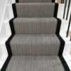 Tapis d'escalier avec motif en chevron noir et blanc et bordure tressée noire, installé sur des volées droites d'escaliers en bois