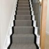 Tapis d'escalier avec motif en chevron noir et blanc et bordure tressée noire, installé sur des volées droites d'escaliers en bois