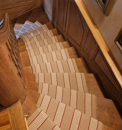 Beige flatweave stair runner with white and red stripes on wooden winding staircase