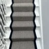 Black and white herringbone flatweave stair runner with a woven black border on a white wooden staircase.