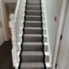 Black and white herringbone flatweave stair runner with a woven black border on a white wooden staircase.