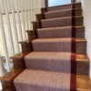 Red herringbone flatweave stair runner with a woven red border installed on a wooden staircase.