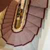 Red herringbone flatweave stair runner with a woven red border installed on a wooden winding staircase.