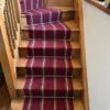 Tapis d’escalier tissé plat à rayures rouges, installé sur un escalier en bois.