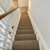 Tapis d’escalier en tissage plat beige sur un escalier en bois peint en blanc.