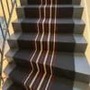 Tapis d'escalier personnalisé en tissage plat noir avec des bandes centrales beige et rouge en motif fermeture éclair, installé sur des escaliers bleus.