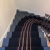 Tapis d'escalier personnalisé en tissage plat noir avec des bandes centrales beige et rouge en motif fermeture éclair, installé sur des escaliers bleus.