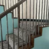 Tapis d'escalier à rayures noires, blanches et grises, installé sur des escaliers en bois et un palier.