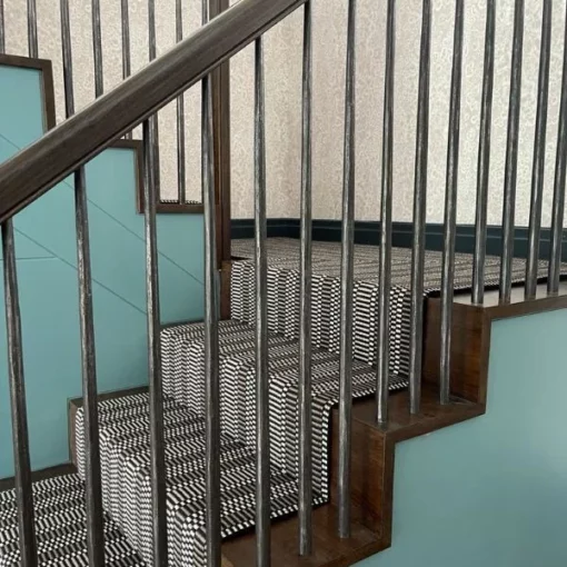 Tapis d'escalier à rayures noires, blanches et grises, installé sur des escaliers en bois et un palier.