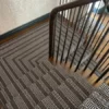 Tapis d'escalier à rayures noires, blanches et grises, installé sur des escaliers en bois et un palier.