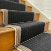 Close-up of a black flatweave stair runner with striped woven border on wooden steps and landing