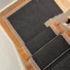 Black flatweave stair runner with striped woven border installed on straight wooden stairs and as a mitred piece on a quarter landing