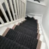 Black flatweave stair runner with woven border installed on white wooden staircase with winding steps
