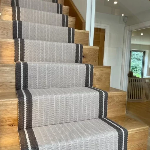 Tapis d’escalier en mastic rayé avec bordure tissée marron, installé sur des escaliers en bois.