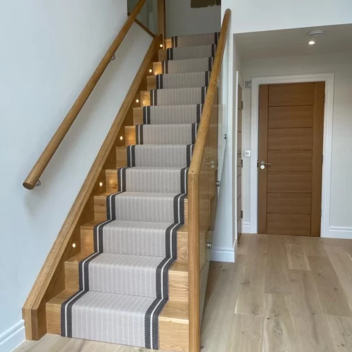 Tapis d’escalier en mastic rayé avec bordure tissée marron, installé sur des escaliers en bois.