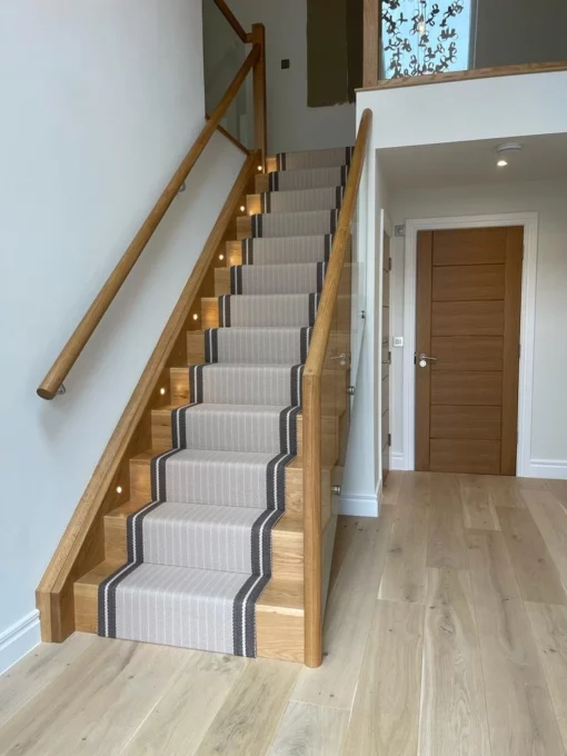 Striped putty stair runner with brown woven border installed on wooden stairs