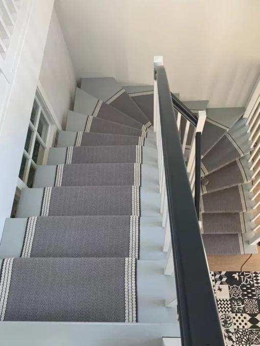 Grey and white stair runner with woven border installed on winding wooden stairs