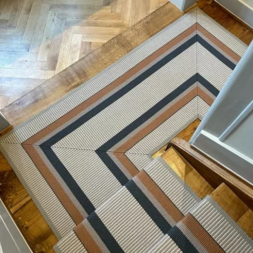 Tapis d'escalier rayé orange, crème et gris installé sur des escaliers et un palier en bois.