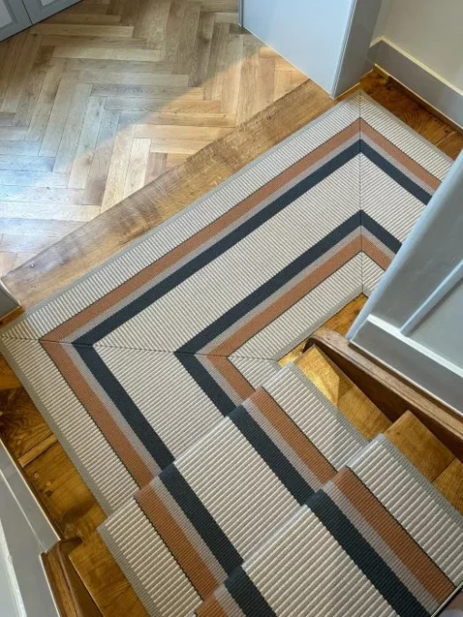 Orange, cream and grey striped stair runner installed on wooden stairs and landing