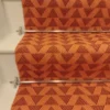 Bright orange stair runner with red triangle pattern on white wooden stairs