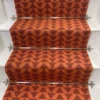 Bright orange stair runner with red triangle pattern on white wooden stairs