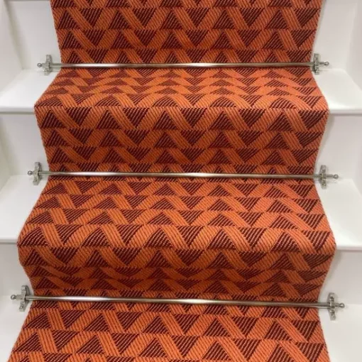 Bright orange stair runner with red triangle pattern on white wooden stairs