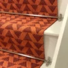 Bright orange stair runner with red triangle pattern on white wooden stairs