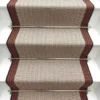 Tapis d’escalier plat ivoire avec bordure tissée orange et grise sur des marches blanches.