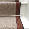 Tapis d’escalier plat ivoire avec bordure tissée orange et grise sur des marches blanches.