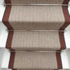 Tapis d’escalier plat ivoire avec bordure tissée orange et grise sur des marches blanches.