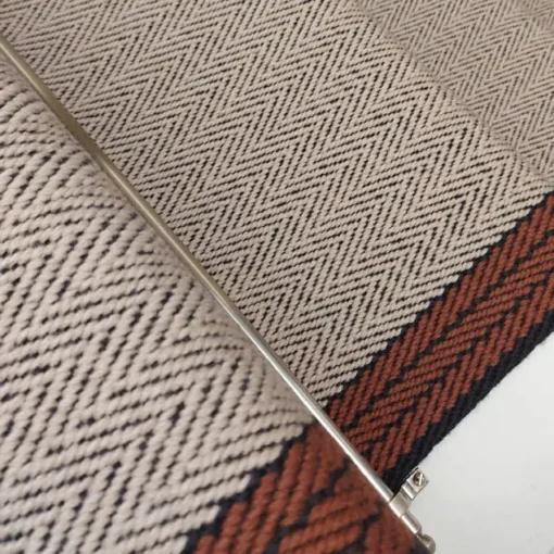 Tapis d’escalier plat ivoire avec bordure tissée orange et grise sur des marches blanches.