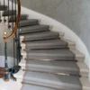 Wide flatweave carpet with woven border and large Diamond pattern installed on a whit winding stone staircase.