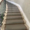 Wide flatweave carpet with woven border and large Diamond pattern installed on a whit winding stone staircase.